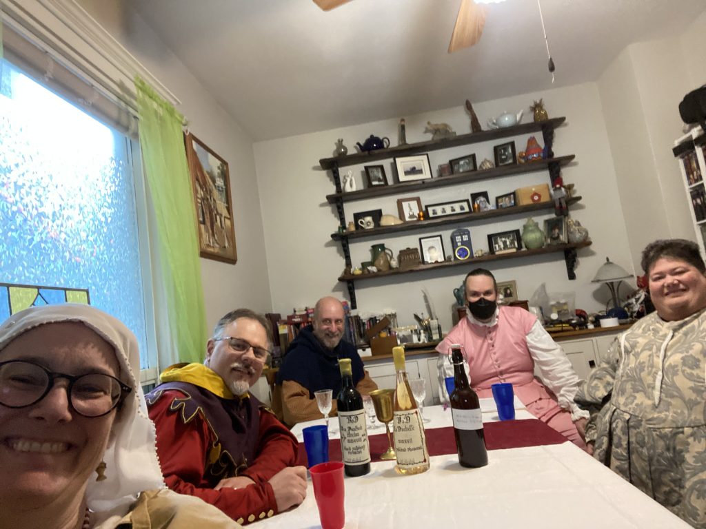 Five smiling people seated around a table with cups. Three bottles are in the center.