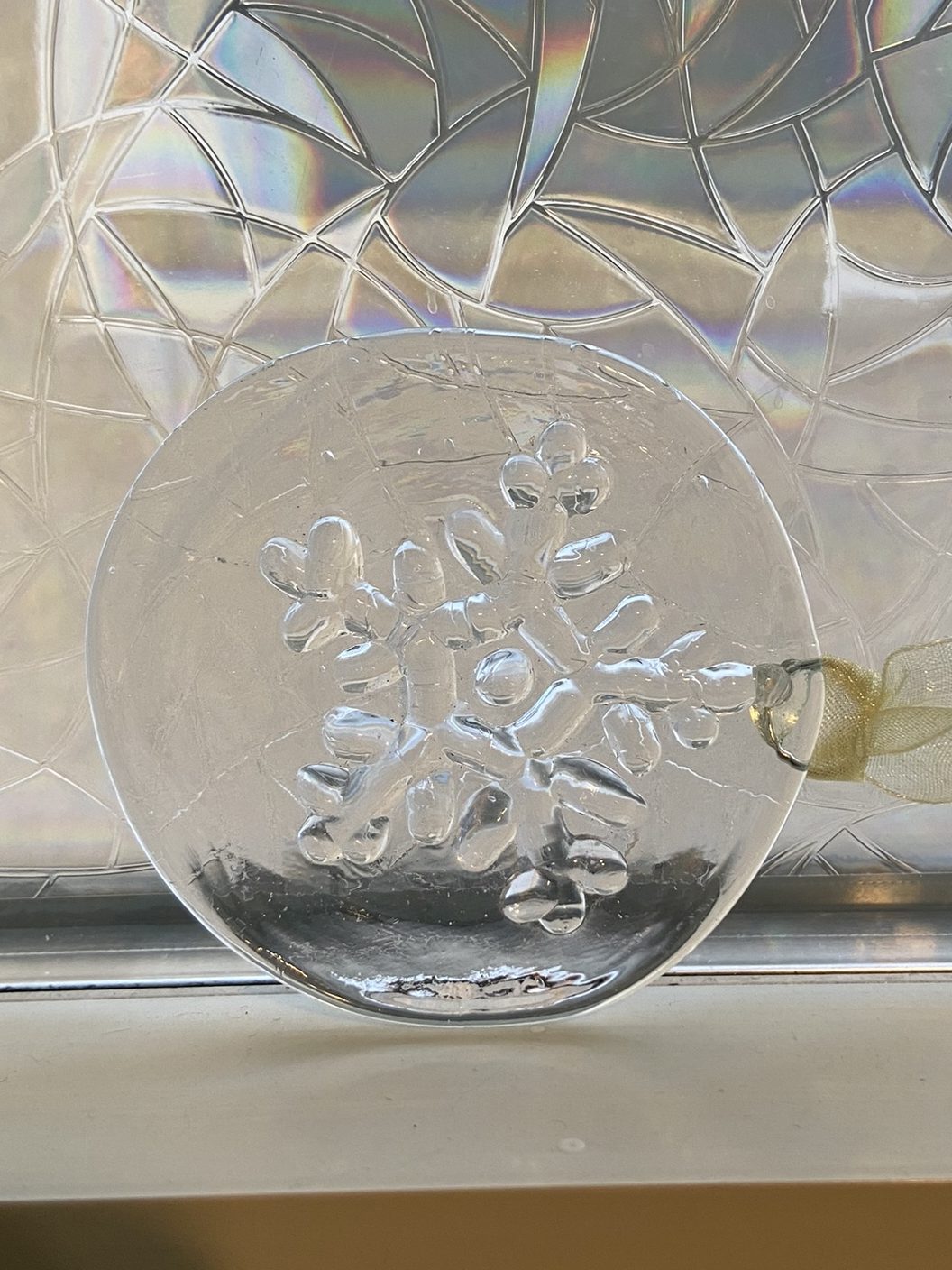 A clear glass disc with a raised snowflake design in front of a window