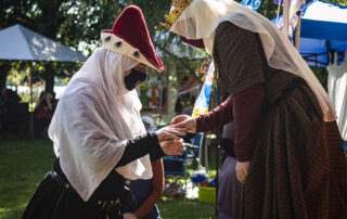 Countess Arlette is given a ring during her elevation by her Majesty Isabel during court, the sunlight illuminates the scene from behind