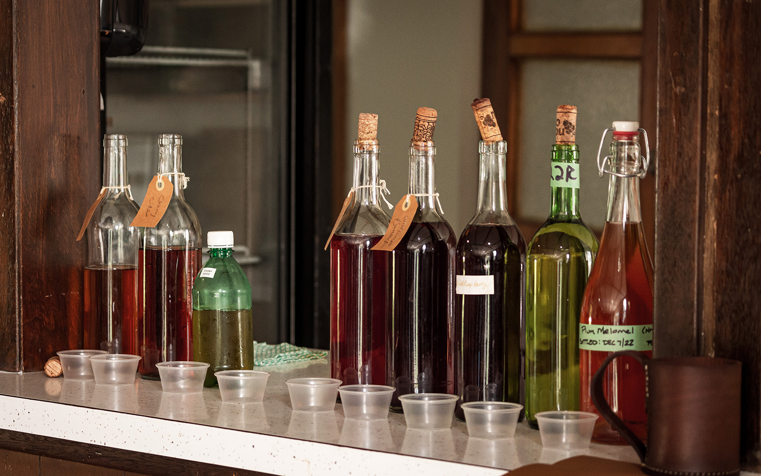 Many coloured bottles of mead, wine, and other alcohols are lined up on a counter to be tasted