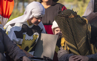 Herald Mabel inquires with Baron Brand about a scroll during evening court