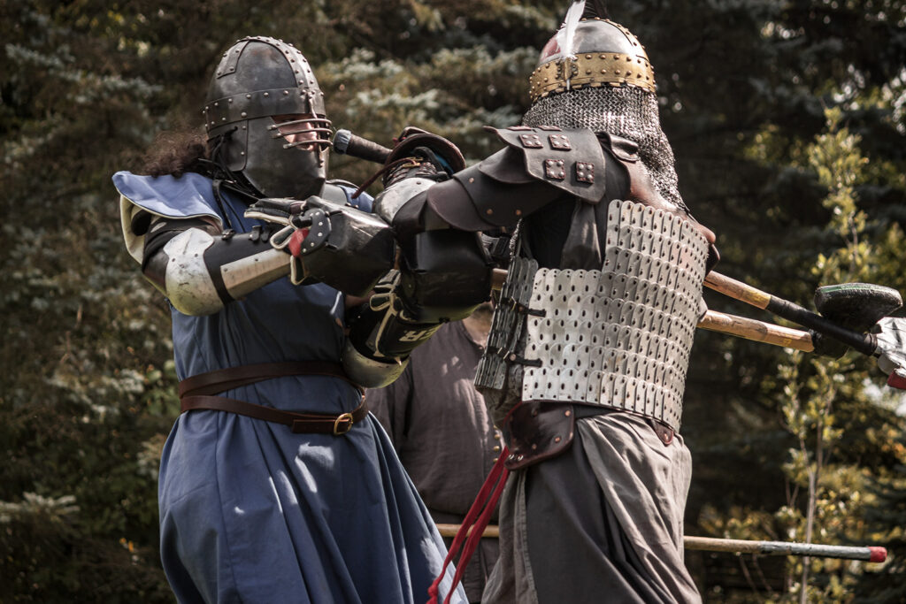 Hespeler in a feathered helmet and lamellar armour and Vivian, dressed in blue with a dark steel helmet, fight up-close during a tournament