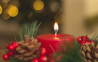 Lit red candle surrounded by pinecones, pine needles, and cranberries