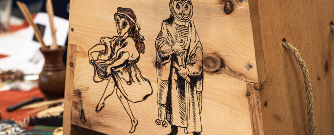 A wooden chest decorated with wood burnings of two owl-headed figures