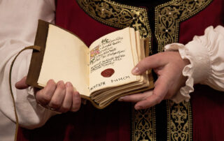 Her Majesty holding open a small leather-bound book. Inside is writing and a red wax seal