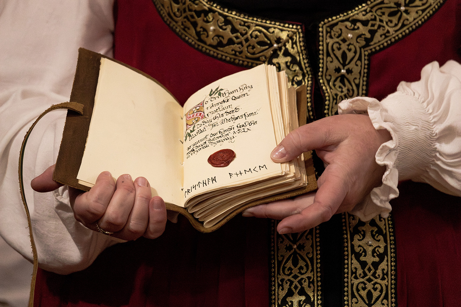 Her Majesty holding open a small leather-bound book. Inside is writing and a red wax seal